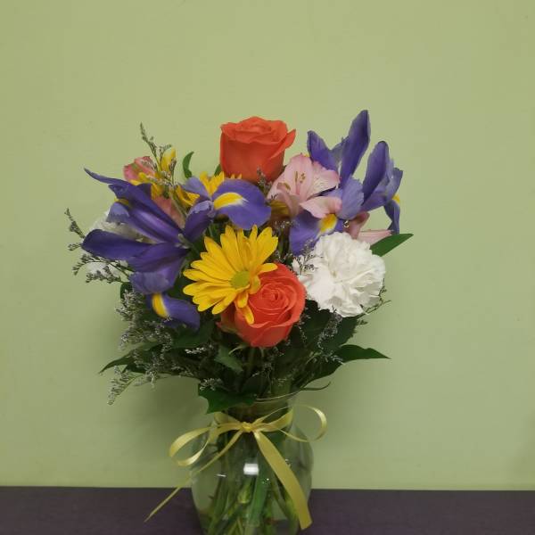 Mixed bouquet of roses, irises, daisies, and carnations in a glass vase