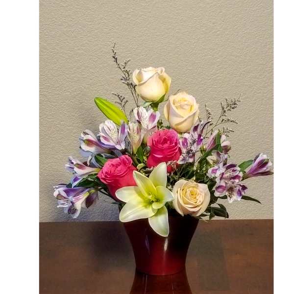 Mixed arrangement of pink and cream roses, lilies, and purple alstroemeria in a red vase