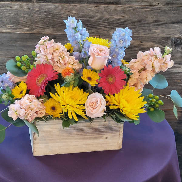 Mixed bouquet in a wooden box with pink, yellow, blue, and red flowers