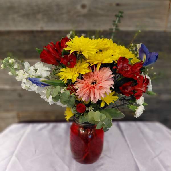 Mixed bouquet in a red glass vase with yellow, red, white, and pink flowers