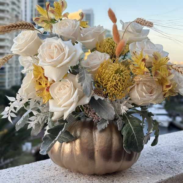 White roses and yellow flowers in a gold pumpkin vase