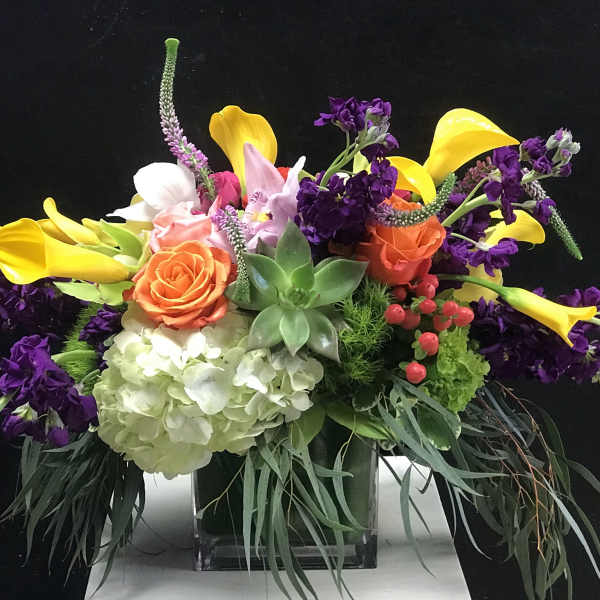 Colorful floral arrangement with calla lilies, roses, hydrangea, and succulents in a glass vase