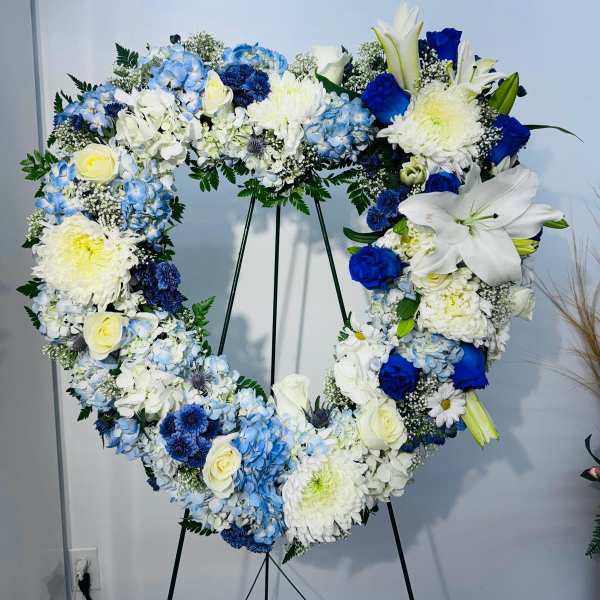 Heart-shaped floral wreath with blue, white, and yellow flowers on a stand