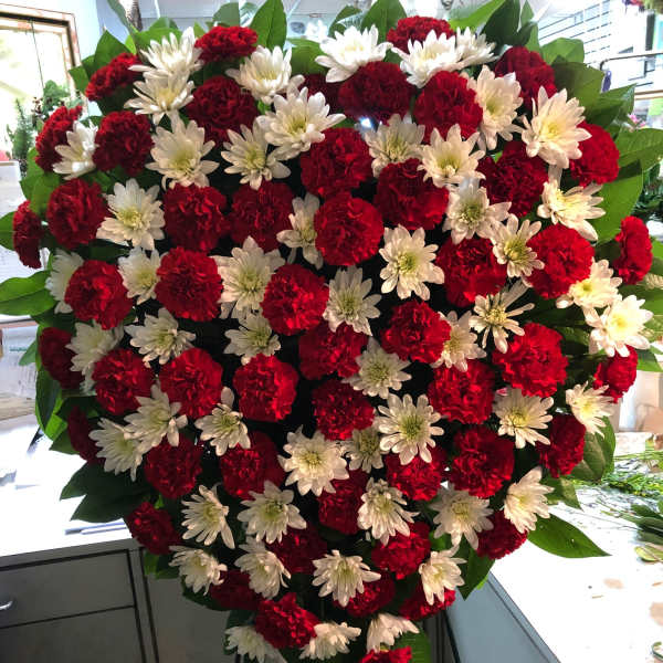 Heart-shaped floral spray of red carnations and white daisies on a stand