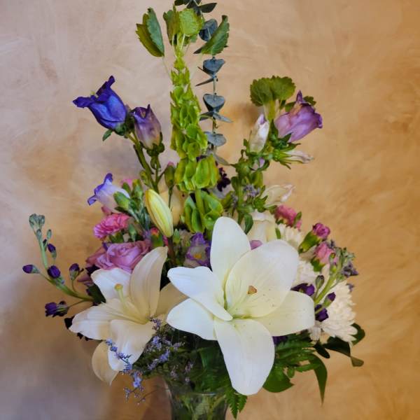 Mixed bouquet of white lilies, purple blooms, and pink roses in a glass vase