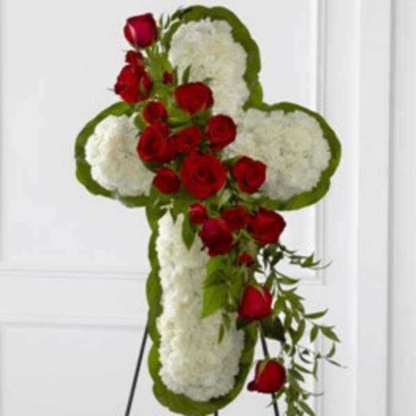 Cross-shaped floral tribute with red roses and white flowers on a stand
