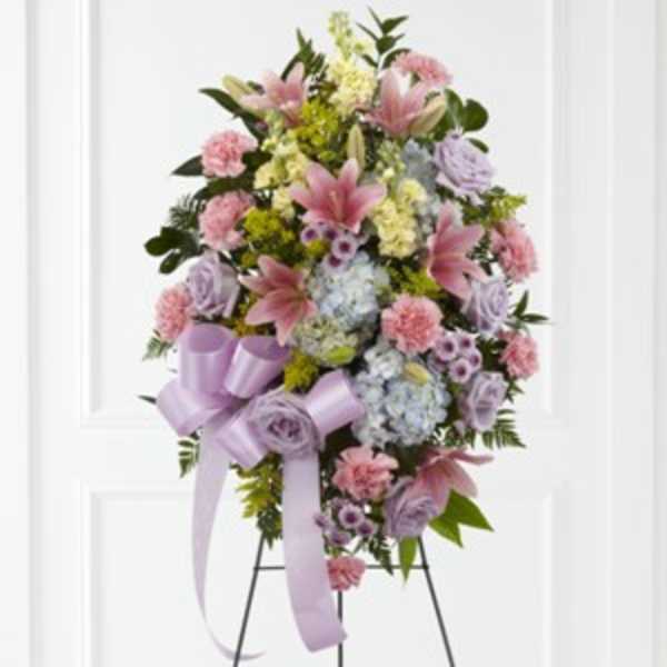 Standing floral spray with pink lilies, carnations, and lavender roses on a ribboned easel