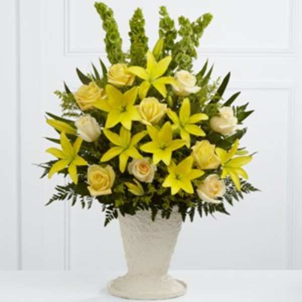 Yellow lilies and cream roses in a white pedestal vase