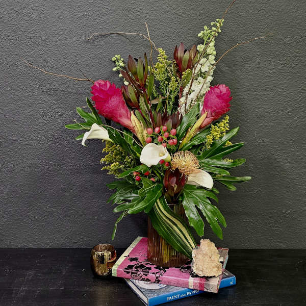 Tropical floral arrangement with pink blooms, white calla lilies, and a glass vase