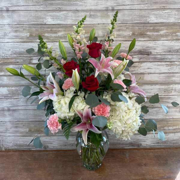 Bouquet of red roses, pink lilies, and white hydrangeas in a glass vase