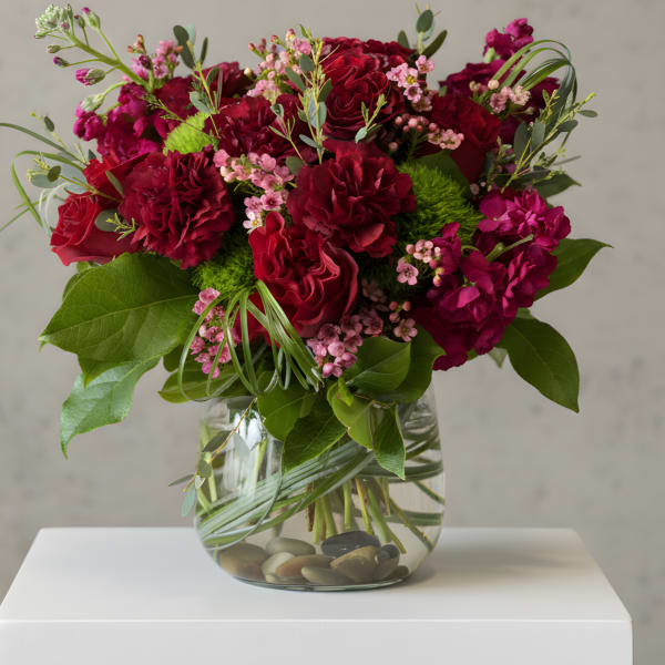 Red and pink bouquet in a clear glass vase with stones