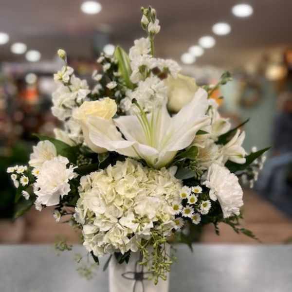 White floral arrangement in a tall vase with lilies and hydrangeas