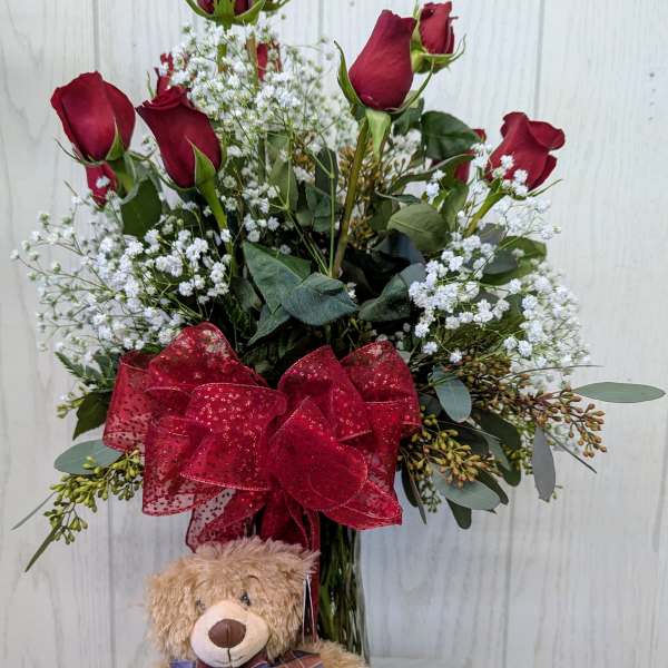 Red roses in a vase with a teddy bear in front