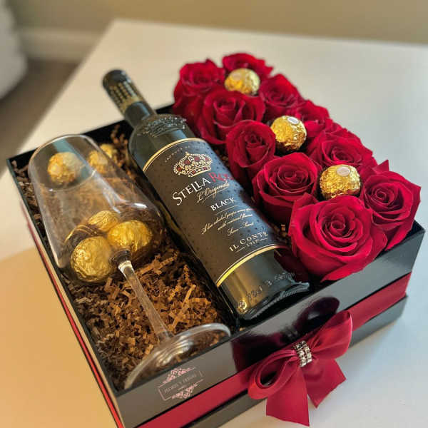 Gift box with red roses, a wine bottle, and a champagne flute with chocolates