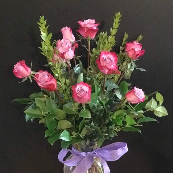 Pink roses in a clear glass vase tied with a purple ribbon