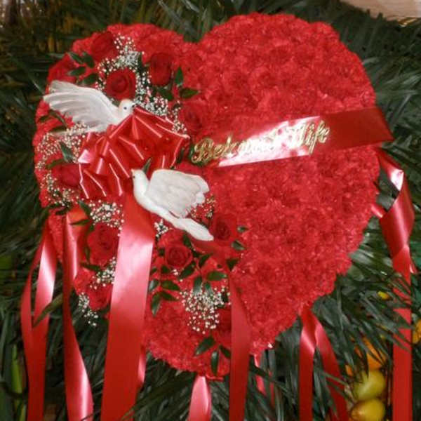 Heart-shaped red floral tribute with roses, ribbons, and white doves