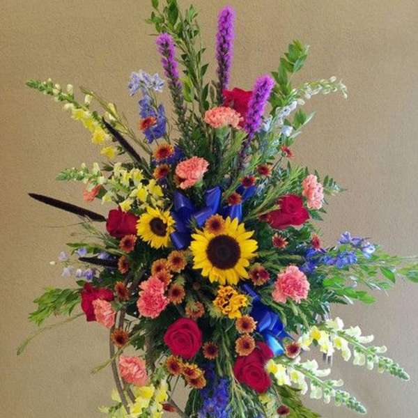 Tall multicolor standing spray with sunflowers, roses, carnations, and snapdragons on an easel