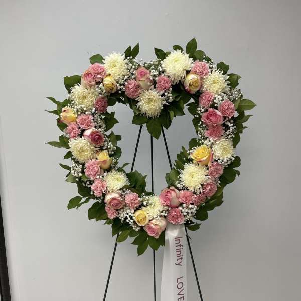 Heart-shaped floral wreath with pink and white flowers on a stand