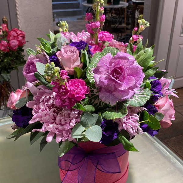 Pink and purple mixed flower arrangement in a round hatbox with ribbon