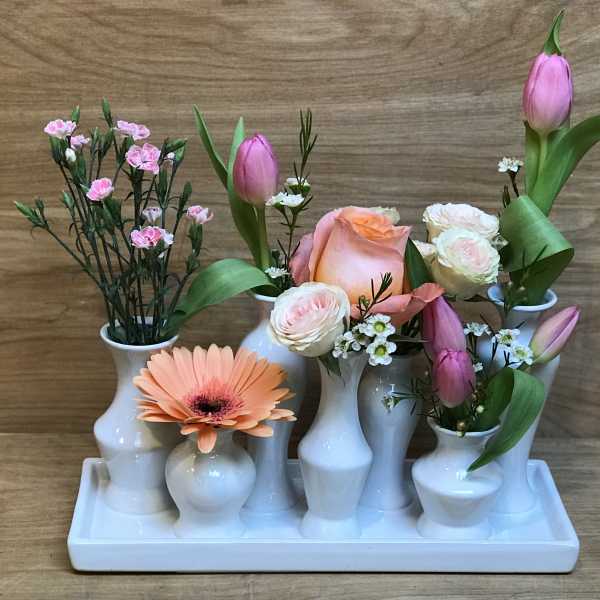 Floral arrangement in white bud vases with pink tulips, roses, and a peach gerbera daisy