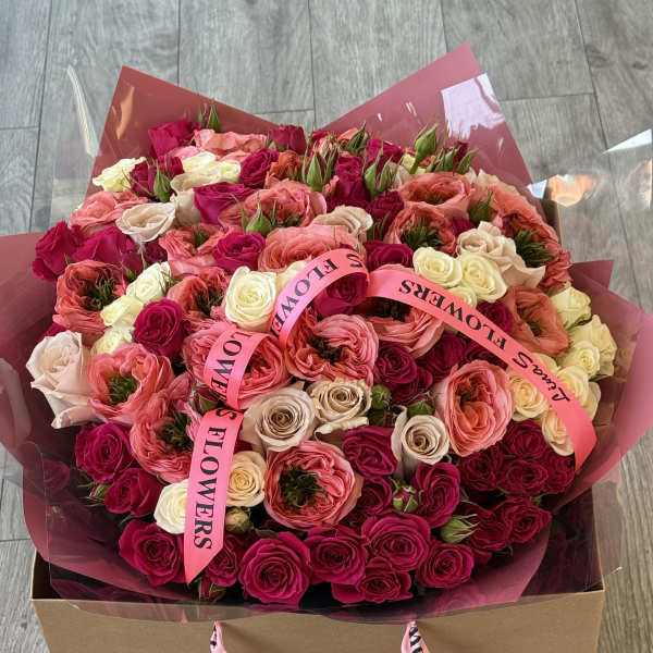 Large bouquet of pink, coral, and cream roses in a box with pink ribbons