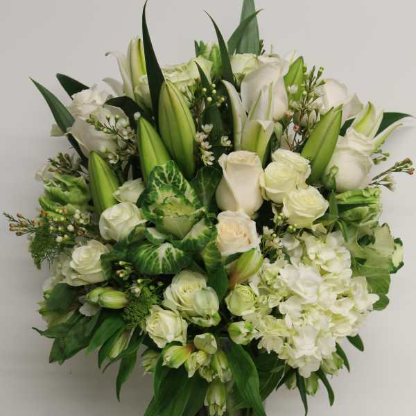 Tall white and green arrangement with roses, lilies, hydrangeas, and alstroemeria in a clear glass vase
