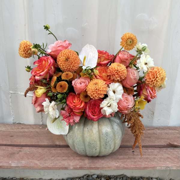 Bouquet of pink, orange, and white flowers in a pale pumpkin vase