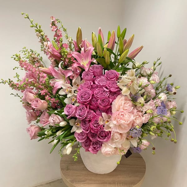 Large pink and white flower arrangement with roses and lilies in a white pot on a table