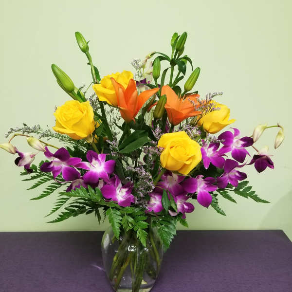 Mixed bouquet of yellow roses, orange lilies, and purple orchids in a glass vase