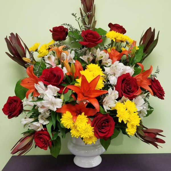 Mixed bouquet of red roses, orange lilies, and yellow chrysanthemums in a white vase