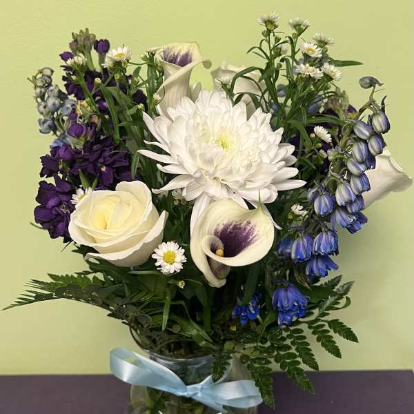 Bouquet of white, purple, and blue flowers in a glass vase with a blue ribbon