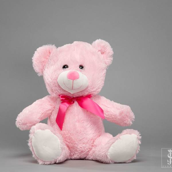 Pink teddy bear with a satin ribbon sitting on a gray background