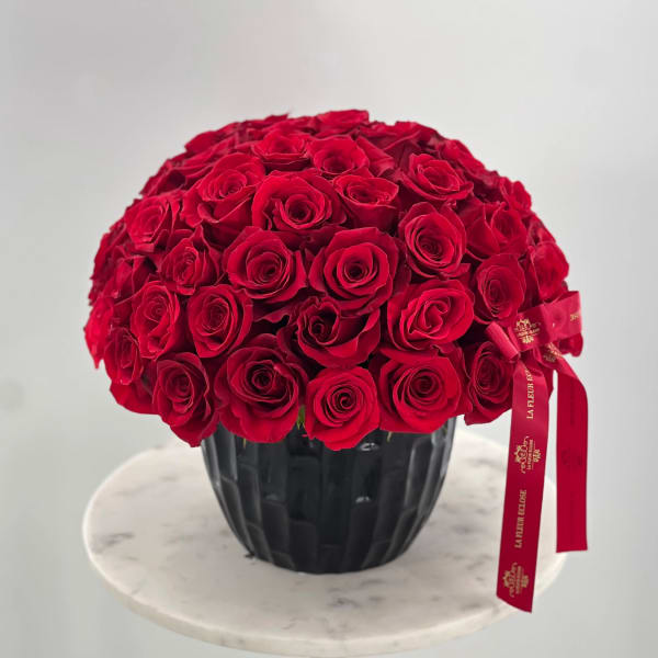 Round bouquet of red roses in a black vase with a red ribbon