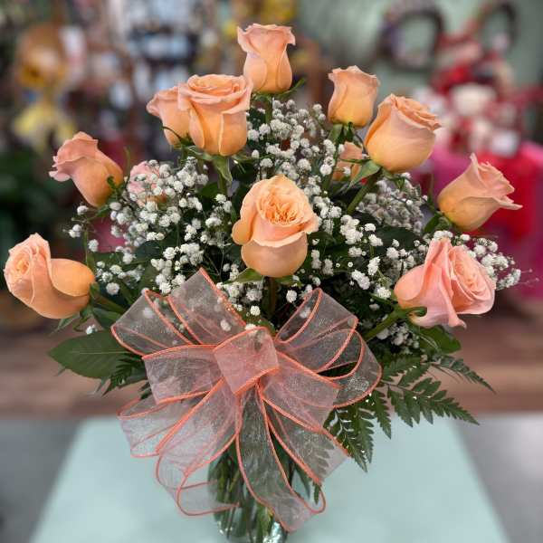 Peach roses in a glass vase with baby's breath and a sheer ribbon bow
