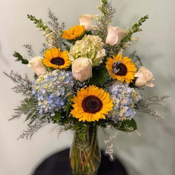 Bouquet of sunflowers, pale roses, and hydrangeas in a glass vase