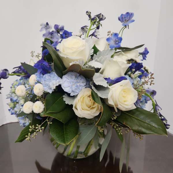 White roses and blue flowers arranged in a glass vase