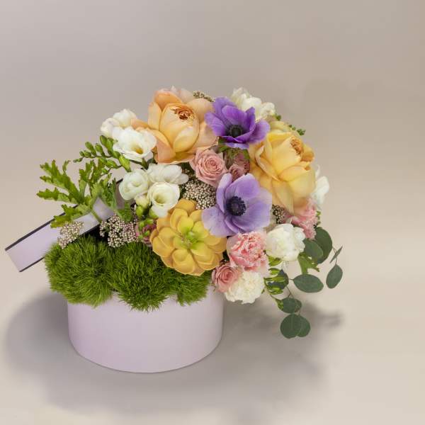 Pastel flower arrangement in a round pink box with purple and peach blooms