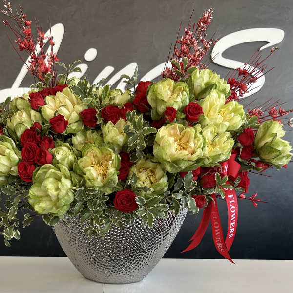 Red roses and green blooms in a silver textured vase with red decorative sprays