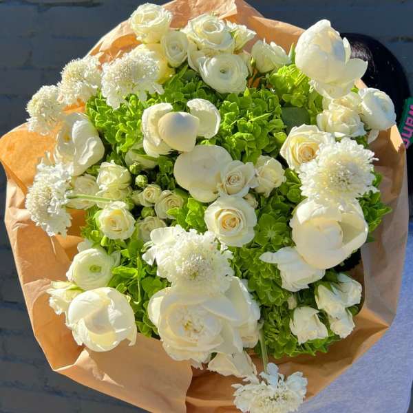 Bouquet of white flowers with bright green hydrangeas wrapped in tan paper