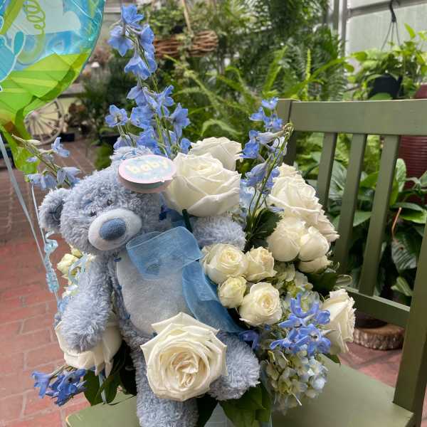 Blue teddy bear with white roses and blue flowers in a vase