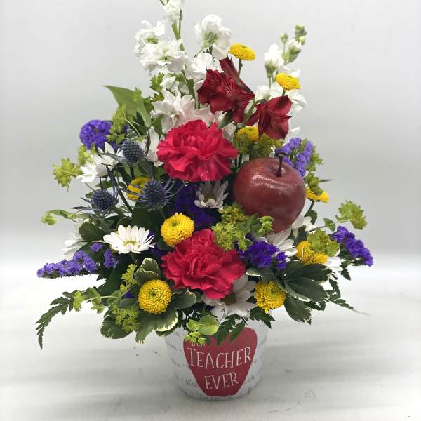 Mixed flower arrangement in a white pot with a "Teacher Ever" label