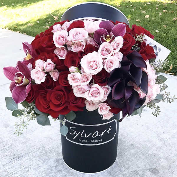 Bouquet of red and pink roses with dark purple orchids in a black hat box