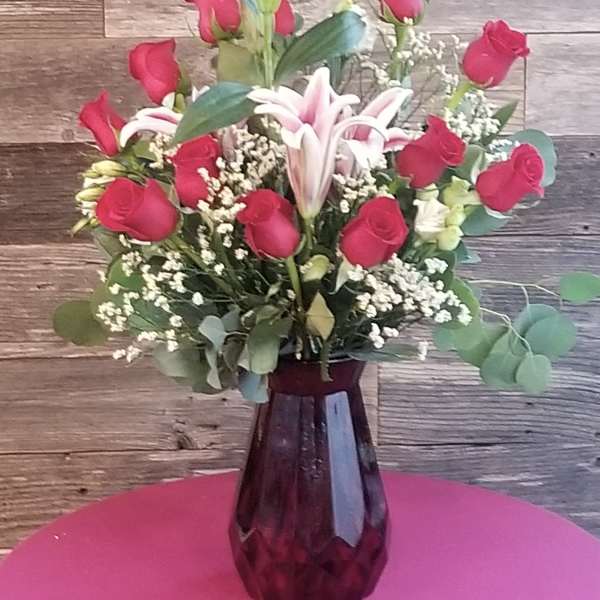 Pink roses and lilies arranged in a purple glass vase