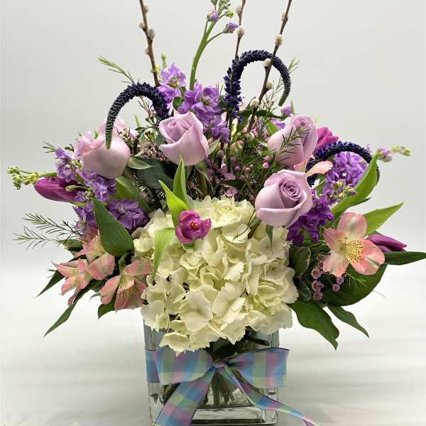 Lavender roses and purple flowers in a glass vase with a plaid ribbon