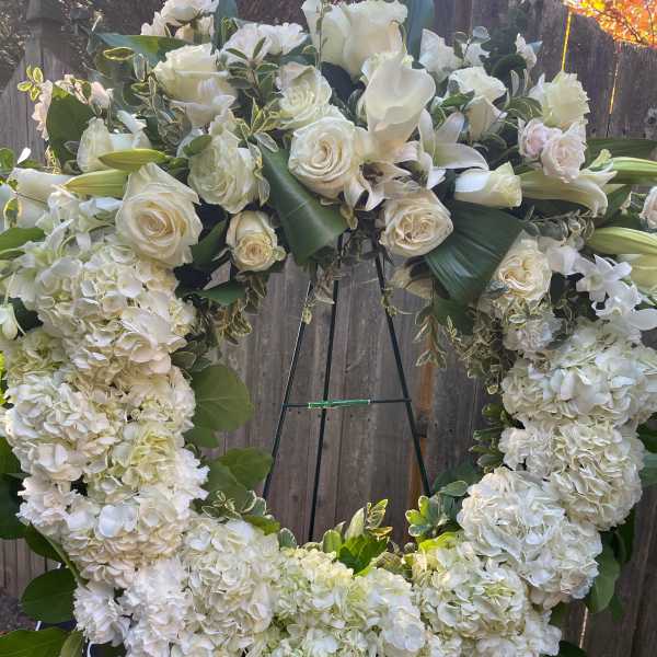 Large white floral wreath on an easel with roses, hydrangeas, and calla lilies
