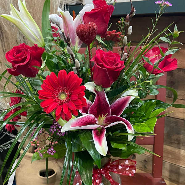 Red roses and pink lilies in a glass vase with a heart ribbon