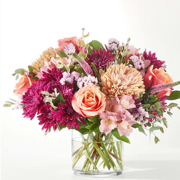 Mixed bouquet of pink, peach, and purple flowers in a clear glass vase