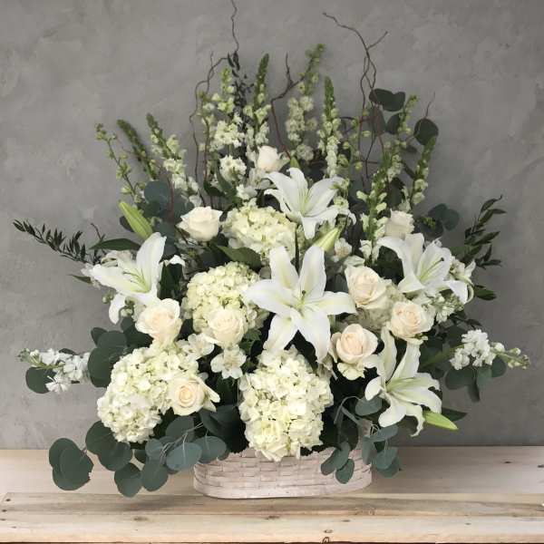 White lilies and cream roses arranged in a basket with greenery