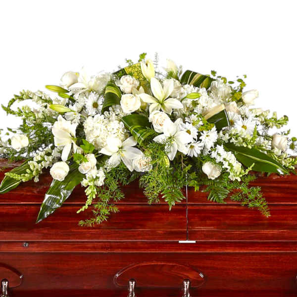 White floral casket spray with lilies and roses on a wooden casket