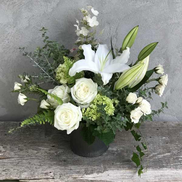 White roses and lilies arranged in a black vase with green accents